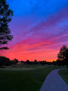 the sun sets over a golf course with trees in the foreground and pink clouds in the sky