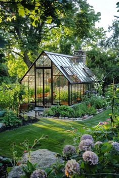 a small greenhouse in the middle of a lush green yard with lots of plants and flowers