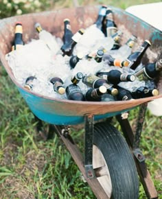 a wheelbarrow filled with bottles of beer sitting on top of a grass covered field