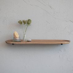 two vases with flowers on a wooden shelf against a white wall, one is filled with water and the other is empty