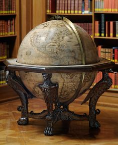 an old globe sits on a stand in front of bookshelves and wooden floors