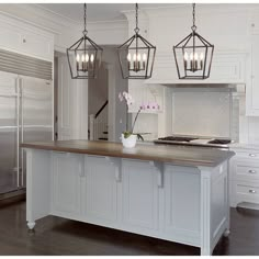 a kitchen with white cabinets and an island in front of the refrigerator, lights hanging from the ceiling