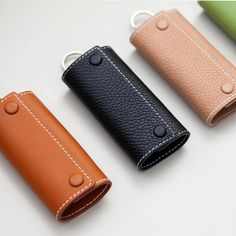 four leather cases are lined up in a row on a white surface, one has a keychain and the other has a clip