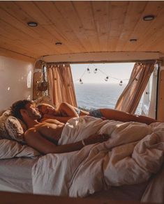 a man and woman laying in bed with the window open to look out at the ocean