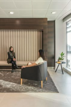 two women are sitting on couches in an office lobby, one is talking to the other