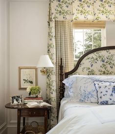 a bed sitting under a window next to a table with a lamp on top of it