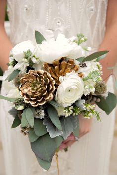 a bridal holding a bouquet of white flowers and pineconis in her hands