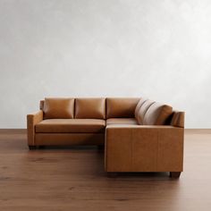 a brown leather couch sitting on top of a wooden floor next to a white wall