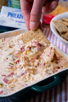 a hand holding a cracker over a bowl of dip with chips on the side