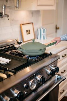 a person holding a frying pan on top of an oven in front of a stove