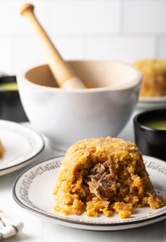 a white plate topped with food next to a bowl filled with soup and a wooden spoon