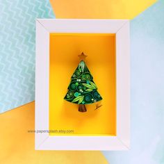 a small green christmas tree in a white frame on a yellow and blue wallpaper