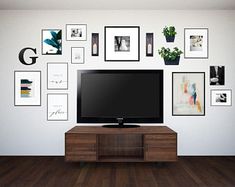 a flat screen tv sitting on top of a wooden cabinet in front of a wall filled with pictures