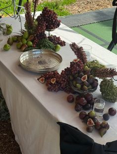 a table with grapes, figs and other fruit on it at an outdoor event