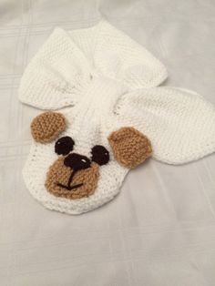 a crocheted teddy bear hat on top of a white bed sheet with black eyes