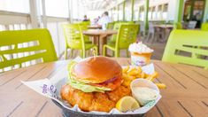 a fish sandwich and french fries on a table at a restaurant with green chairs in the background