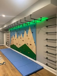 there is a climbing wall in the room that has a blue mat and some green lights