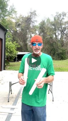 a man in green shirt and sunglasses holding up a white object with scissors on it