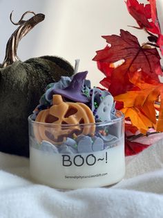 a candle that is sitting next to some pumpkins and leaves on a white blanket