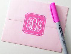 a pink envelope with a monogrammed sticker on it and a pen next to it