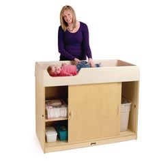 a woman standing next to a baby in a crib on top of a wooden cabinet