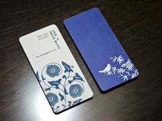 two business cards sitting next to each other on a wooden table with blue and white designs