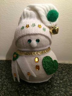 a white stuffed animal with green and gold decorations on it's head, sitting next to a wall