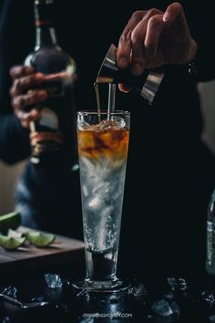 the bartender is pouring an alcoholic drink into a tall glass with ice and lime wedges