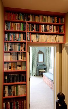 a bookshelf filled with lots of books next to a doorway leading to a bed