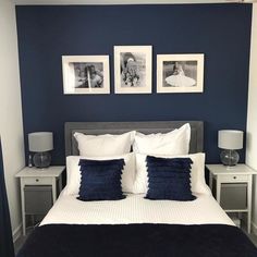 a bed with white and blue pillows in a bedroom next to two pictures on the wall