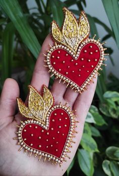 two red and gold heart shaped brooches with golden wings on them, sitting next to each other