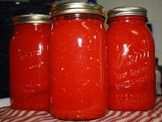 three red jars are lined up on a striped table cloth, one is filled with liquid