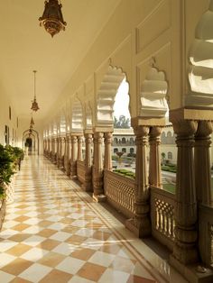 a long hallway with columns and plants on the side walk in front of it is an ornate chandelier that hangs from the ceiling