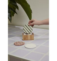 a person holding a green and white striped coaster on top of a wooden stand next to a potted plant