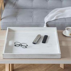 a tray with glasses, remote control and coffee cup on it next to a couch