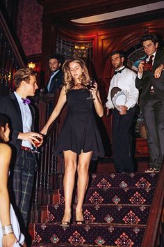 a woman in a short black dress is walking down the stairs while two men are standing behind her