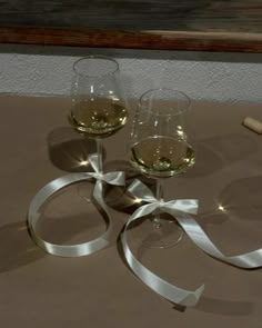 two glasses of wine are sitting next to each other on a table with white ribbon