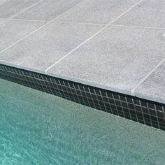 an empty swimming pool with tiled walls and blue water in the foreground, on a sunny day