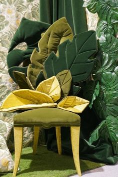 a green chair sitting in front of a wall with plants on it and curtains behind it