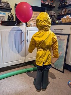 a child in a yellow raincoat standing next to a green hose and red balloon