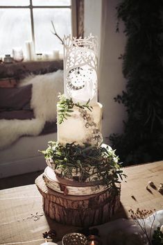 a three tiered cake sitting on top of a wooden table next to a window