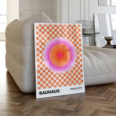 an orange and pink poster sitting on top of a wooden floor next to a white couch