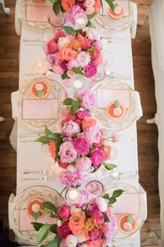 the table is set with pink and orange flowers, candles and place settings on it