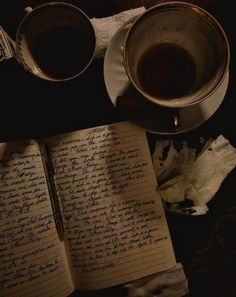 an open book with writing on it next to two cups of coffee