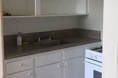 an empty kitchen with white cabinets and gray counter tops, along with a stove top oven