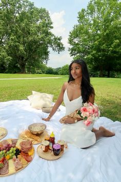 a woman sitting at a table with food and drinks in front of her on the grass