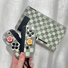 a hand holding two nintendo wii controllers in front of a checkerboard design case