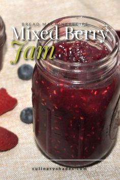 a mason jar filled with mixed berry jam next to strawberries and raspberries