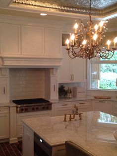 a chandelier hanging from the ceiling in a kitchen with white cabinets and marble counter tops