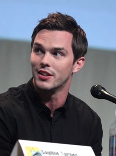 a man sitting at a table with a microphone in front of him and looking off to the side